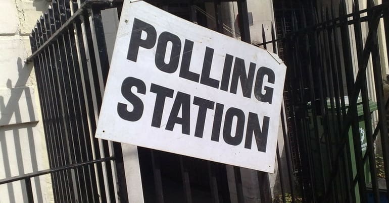 A polling station sign on a fence