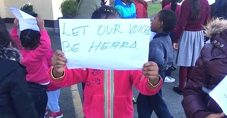 Photo of a child at the protest of asylum seekers in Ireland holding up a sign that says "Let our voices be heard".