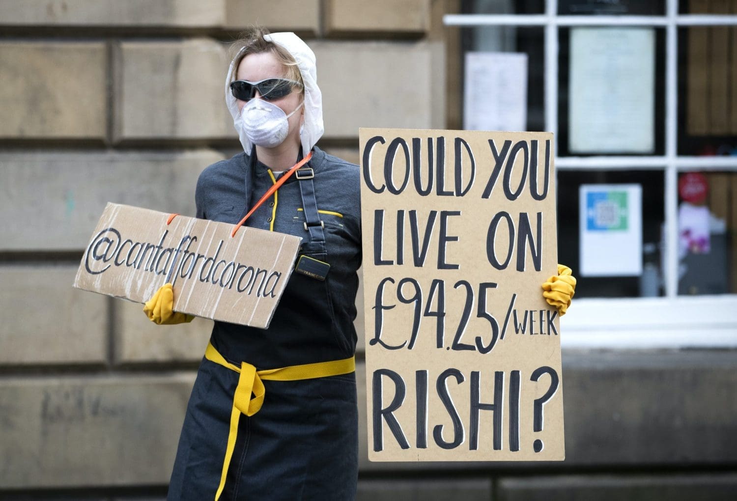 A woman holding a placard that reads 'Could you live on £94.25 an hour Rishi'