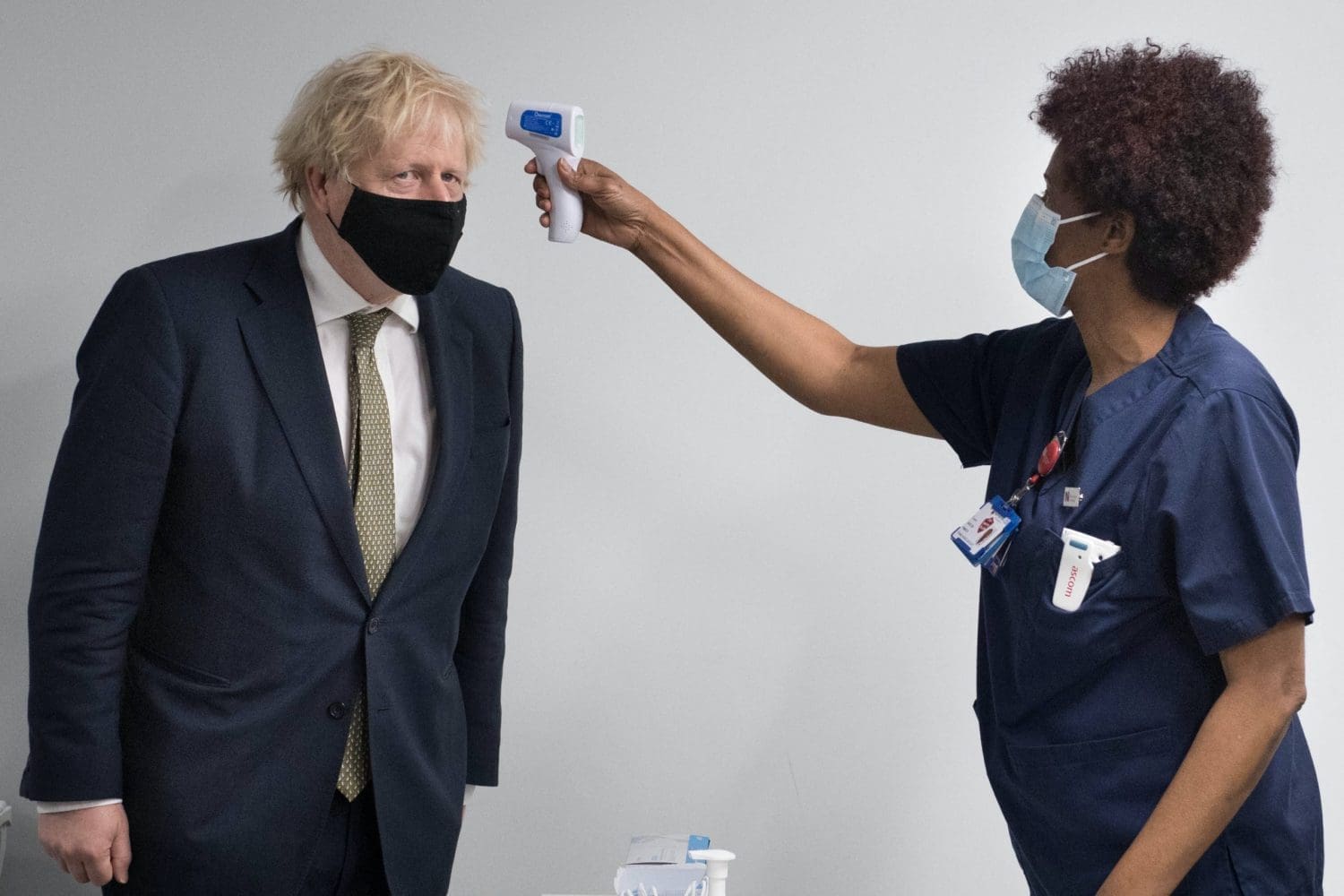Boris Johnson wearing a mask having his temperature taken by a nurse