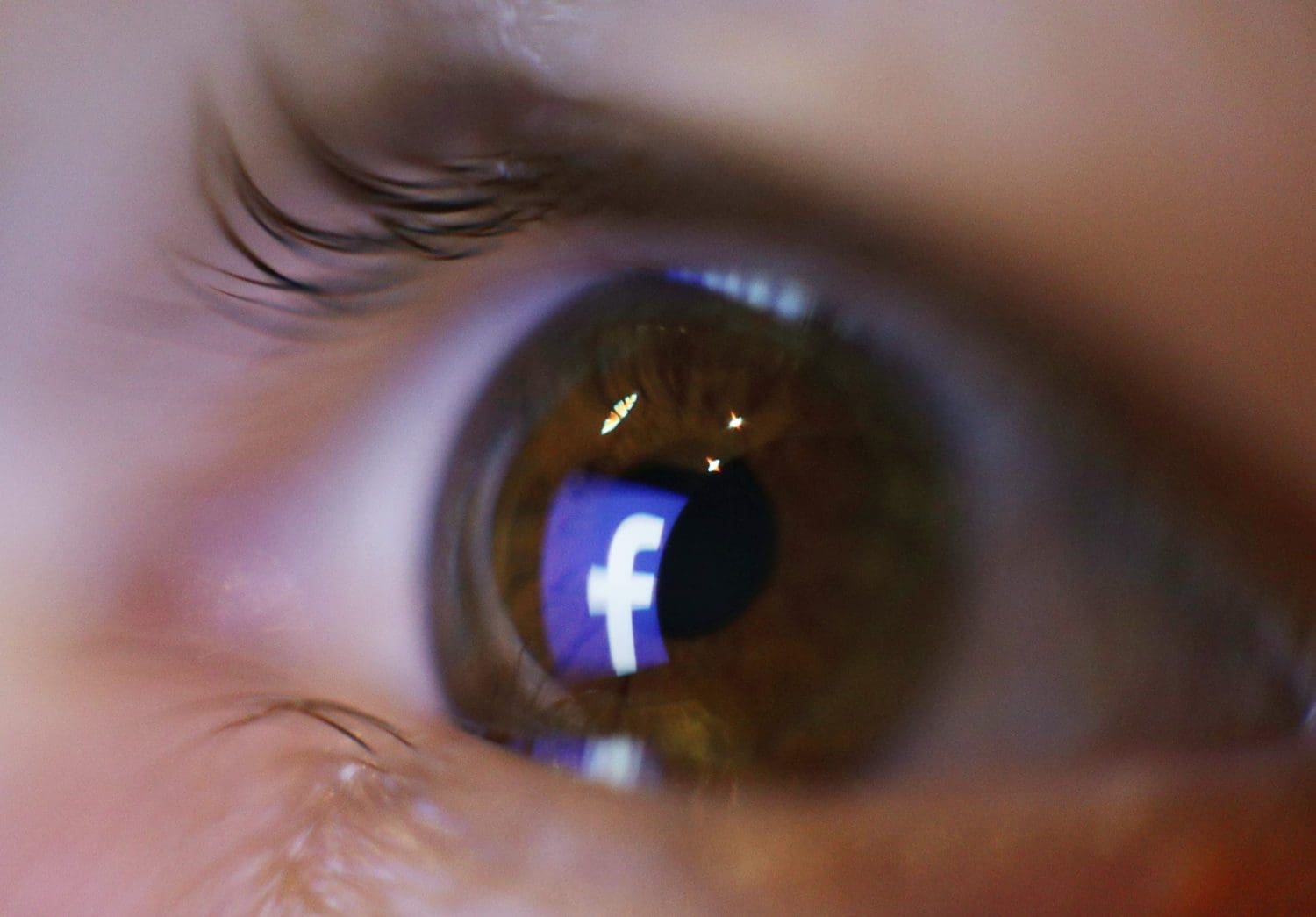 An eyeball with the Facebook logo reflecting in it