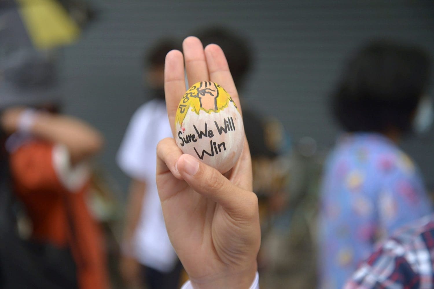 A protestor holding an egg with 'we will win' written on it