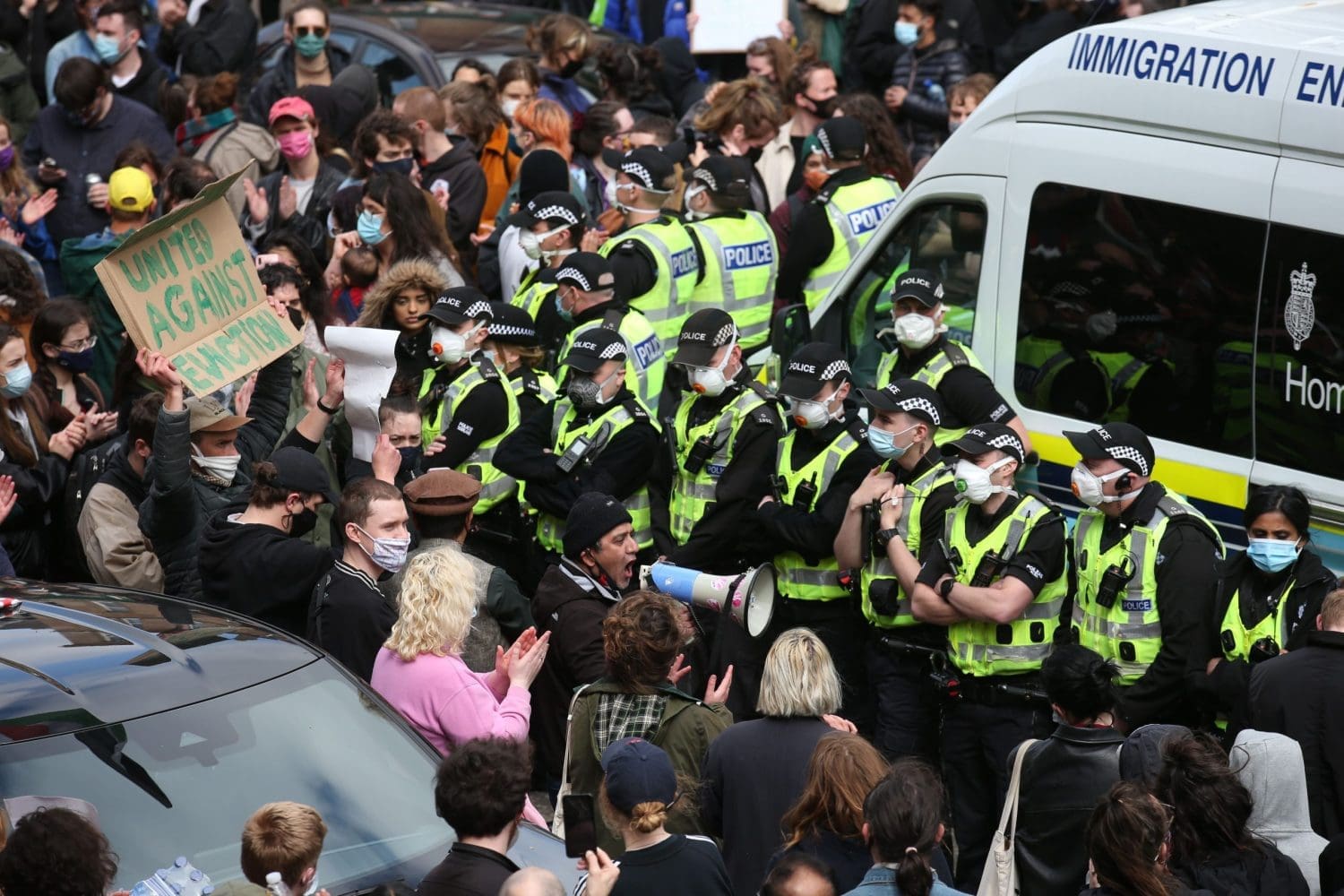 A ring of police officers dwarfed by a crowd of people supporting the men arrested
