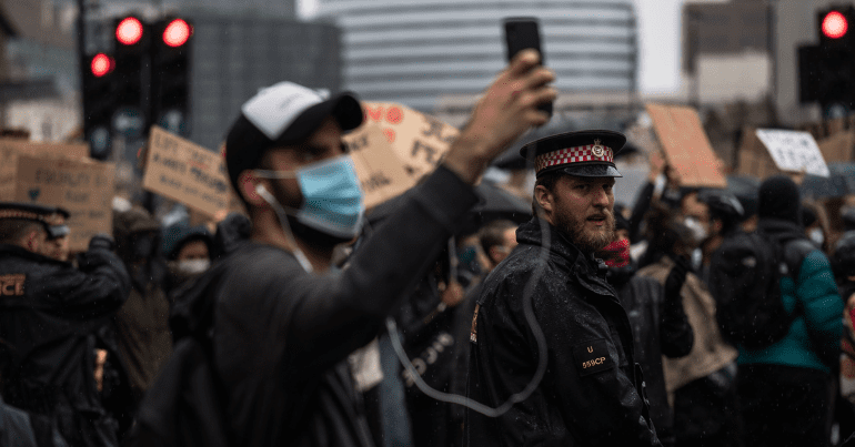 A protestor records on his phone while a police officer looks on during a protest - public order bill going through the House of Lords
