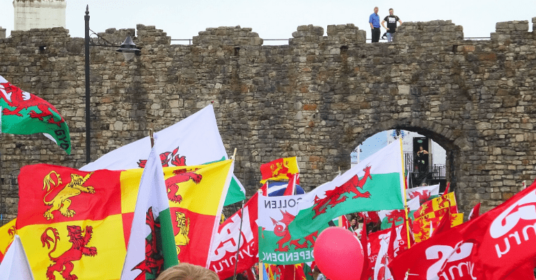 Welsh independence supporters waving banners in front of a castle in Wales, YesCymru