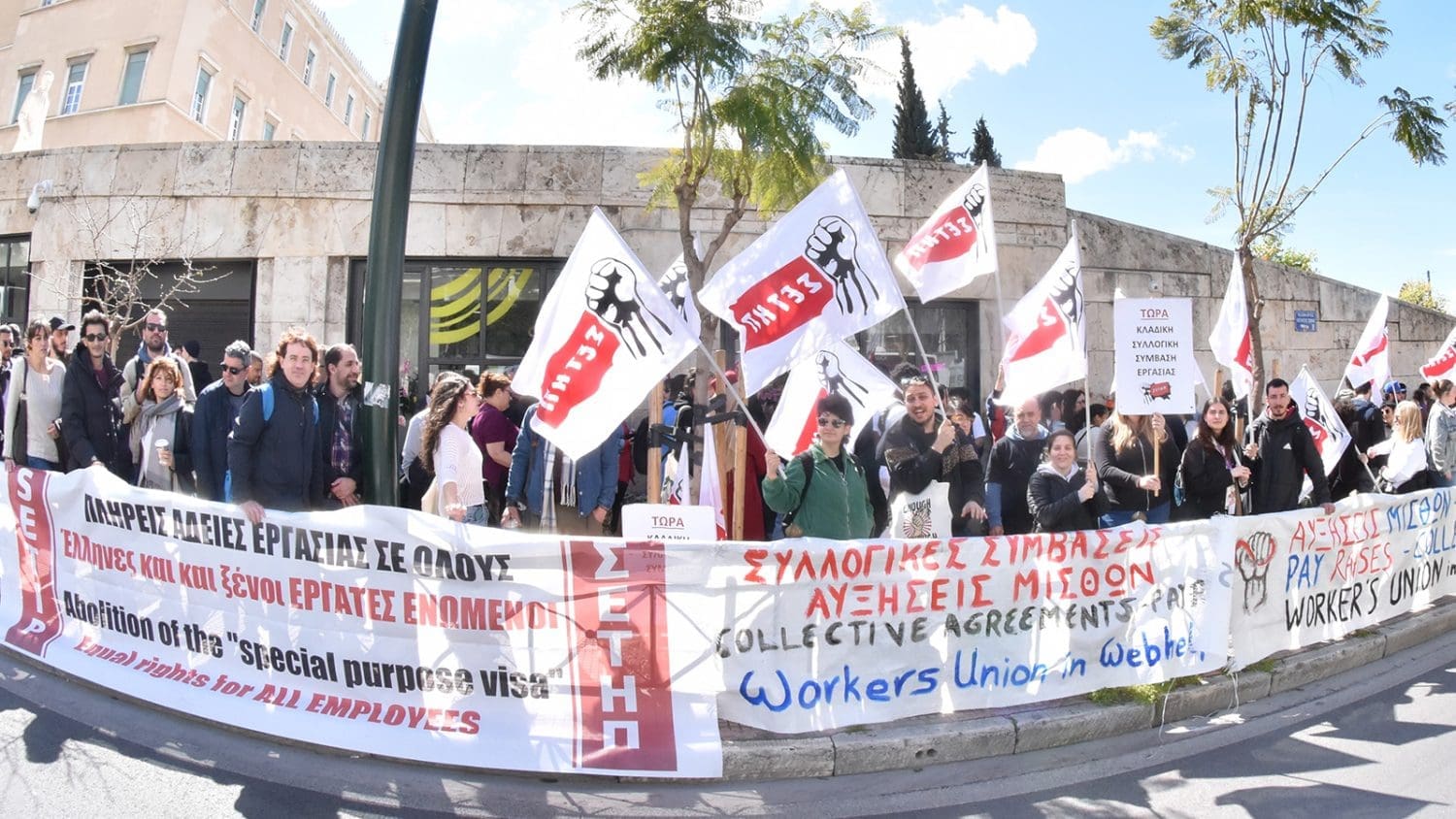 a group of striking Greek call centre workers waving flags and holding banners