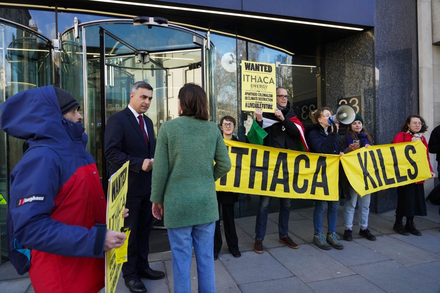Activists engage with employees as they enter Ithaca's offices. Banner reads: "Ithaca Kills".