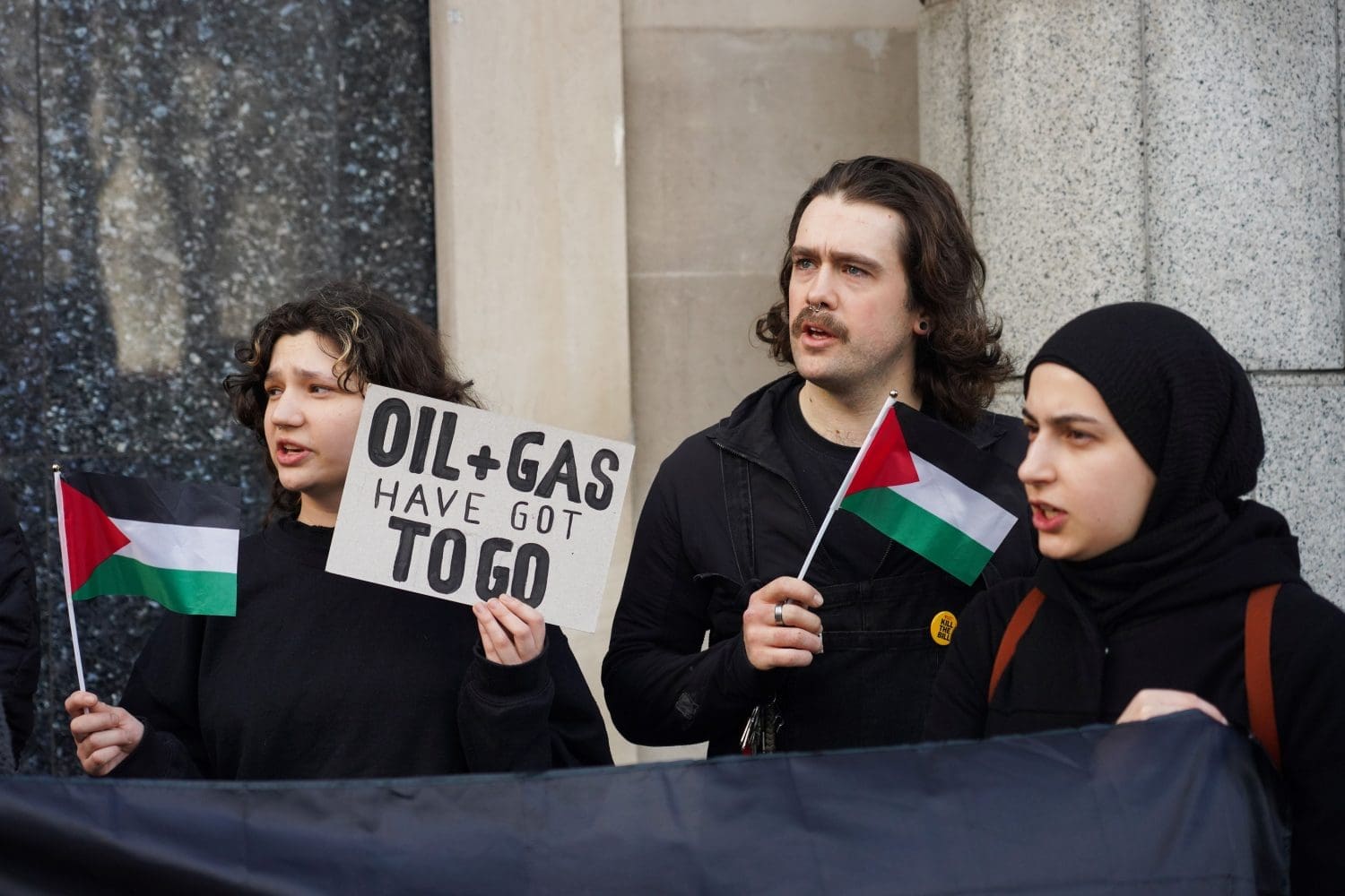 Activists hold Palestinian flags and a placard that reads "Oil + gas have got to go"