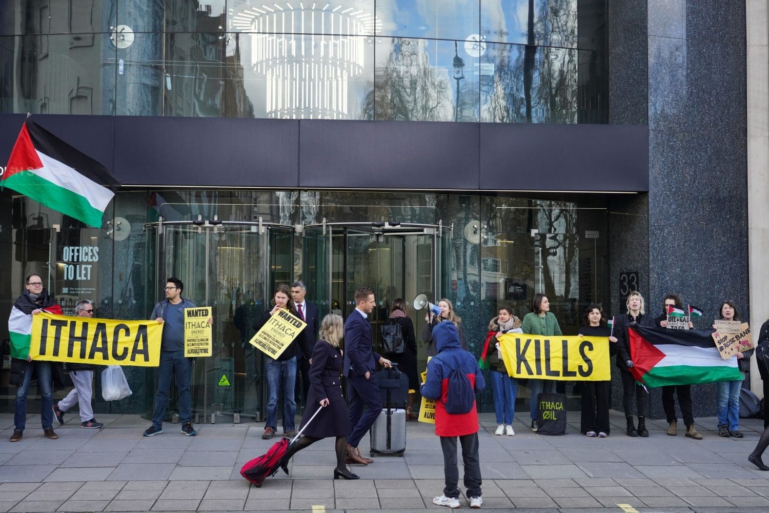 Actvists hold Palestinian flags and a banner which reads "Ithaca Kills" outside the company's London office building. 