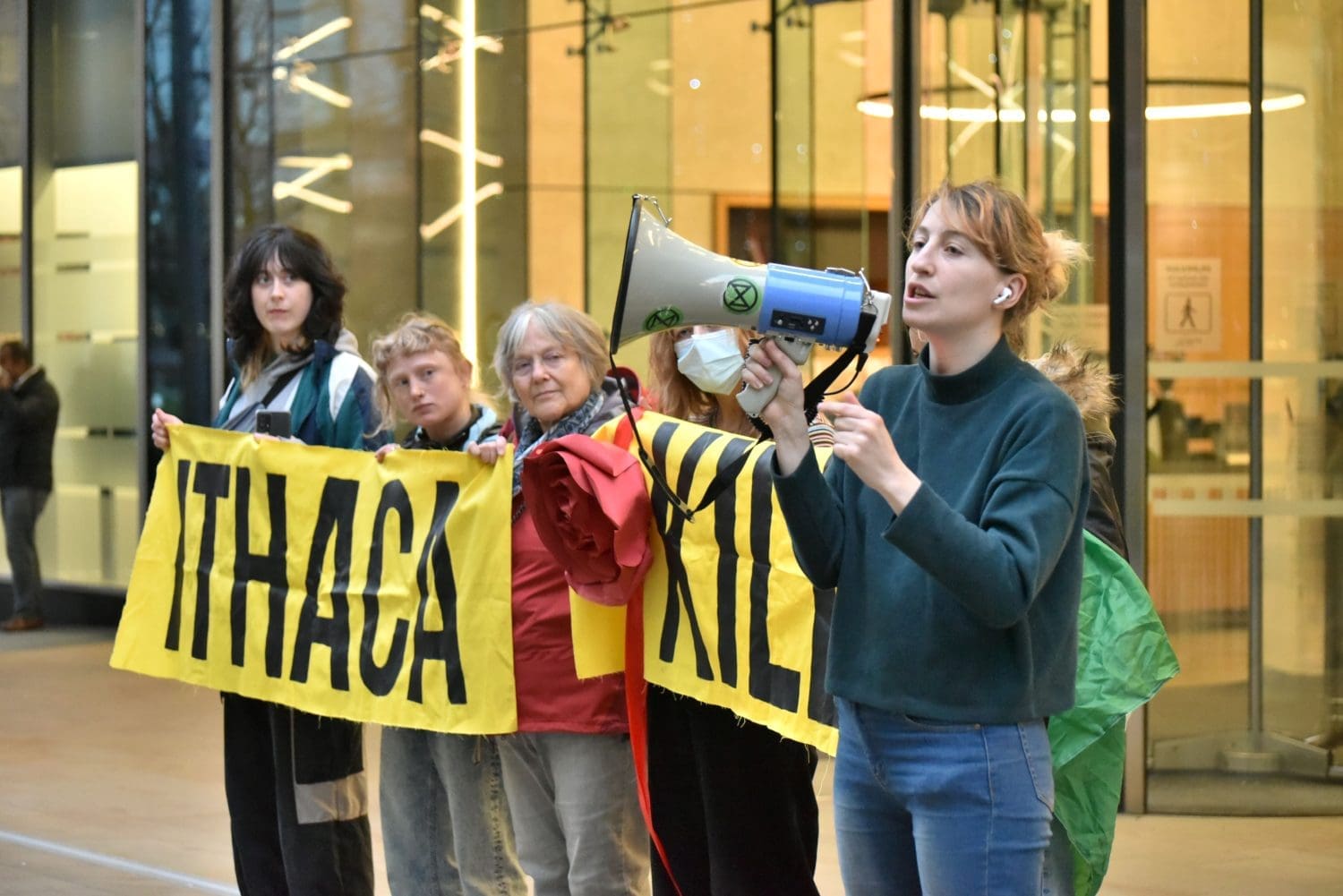 Fossil Free London activists stand in a line in front of Equinor's entrance at Paddington. One holds a megaphone, while the rest raise a banner which reads "Ithaca Kills".