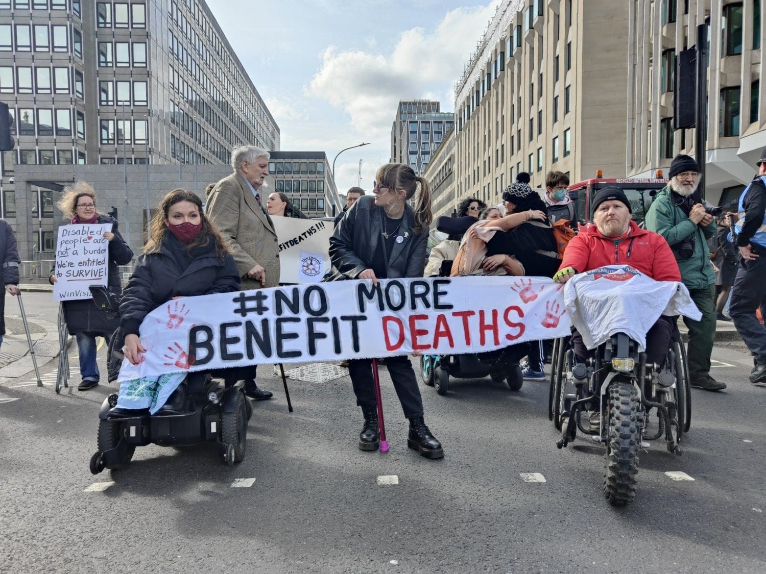 people holding a sign reading 'no more benefit deaths' DPAC DWP