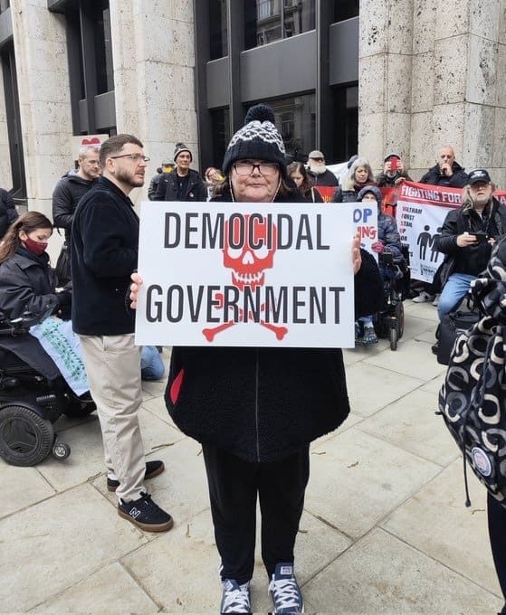 Paula Peters holding a sign saying "democidal government" DWP DPAC