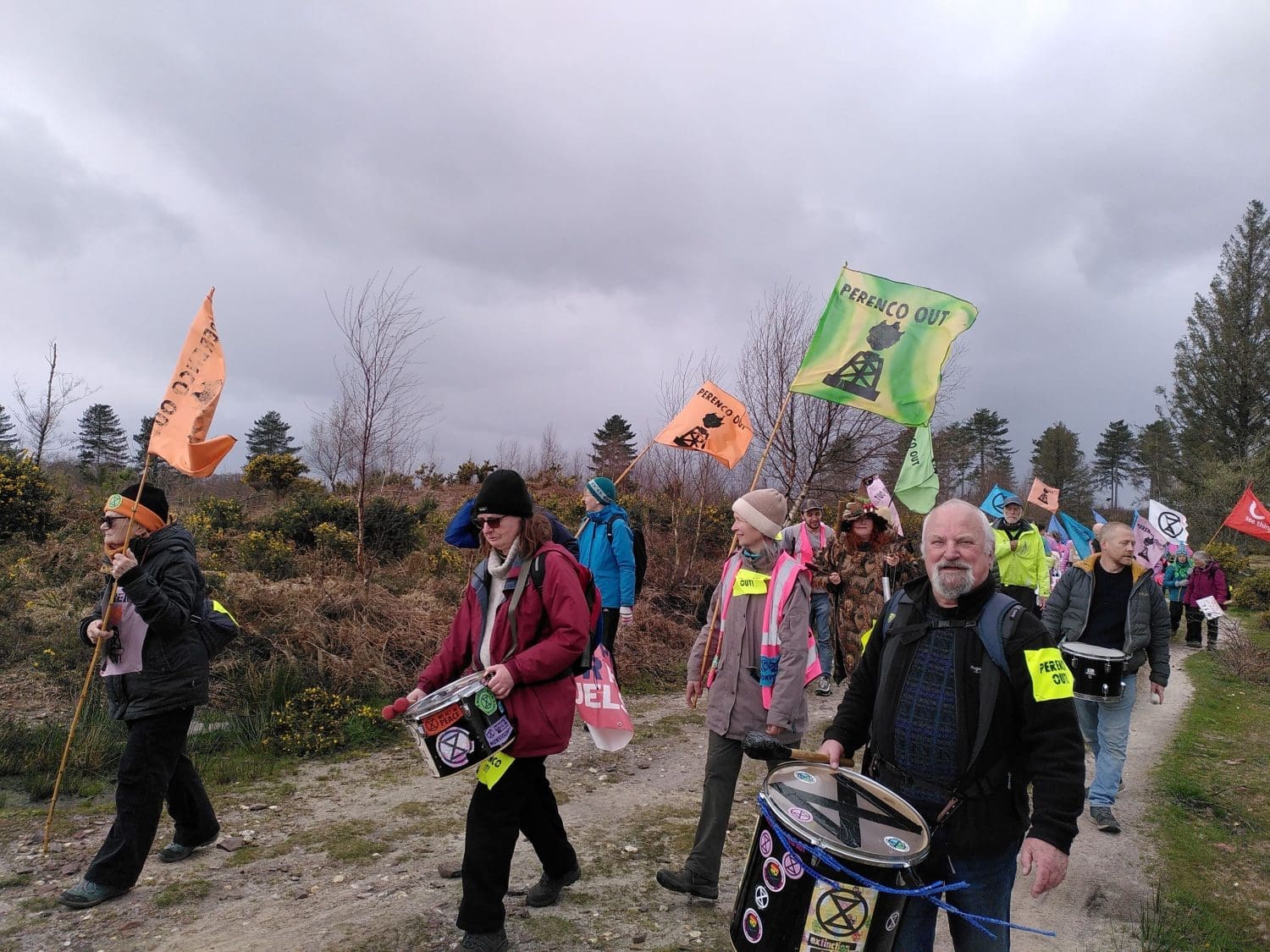 Protesters march with drums and "Perenco out" flags across the lowland heath. 