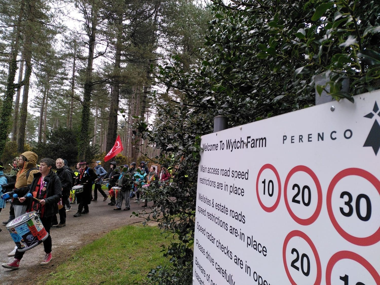 Protesters turn the corner to Wytch Farm's entrance. Perenco Wytch Farm sign in the foreground.