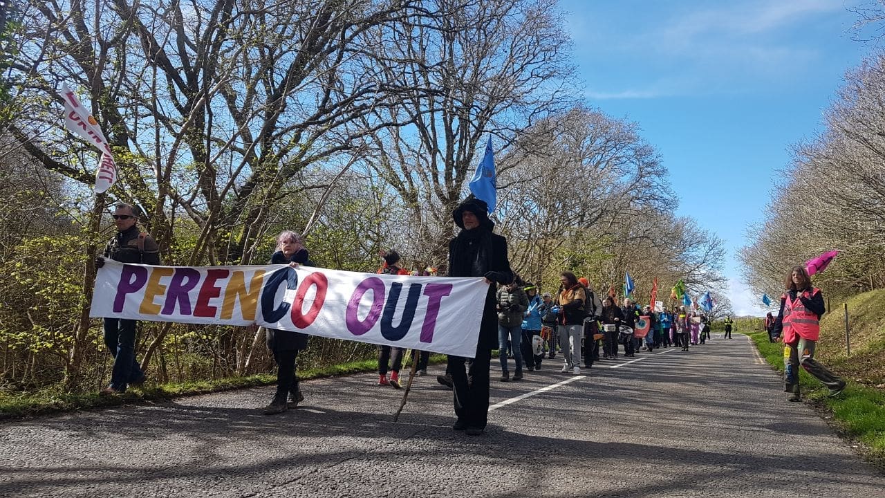 Protesters march along a road towards Perenco's Wytch Farm oil field. They carry a banner that reads: "Perenco Out"