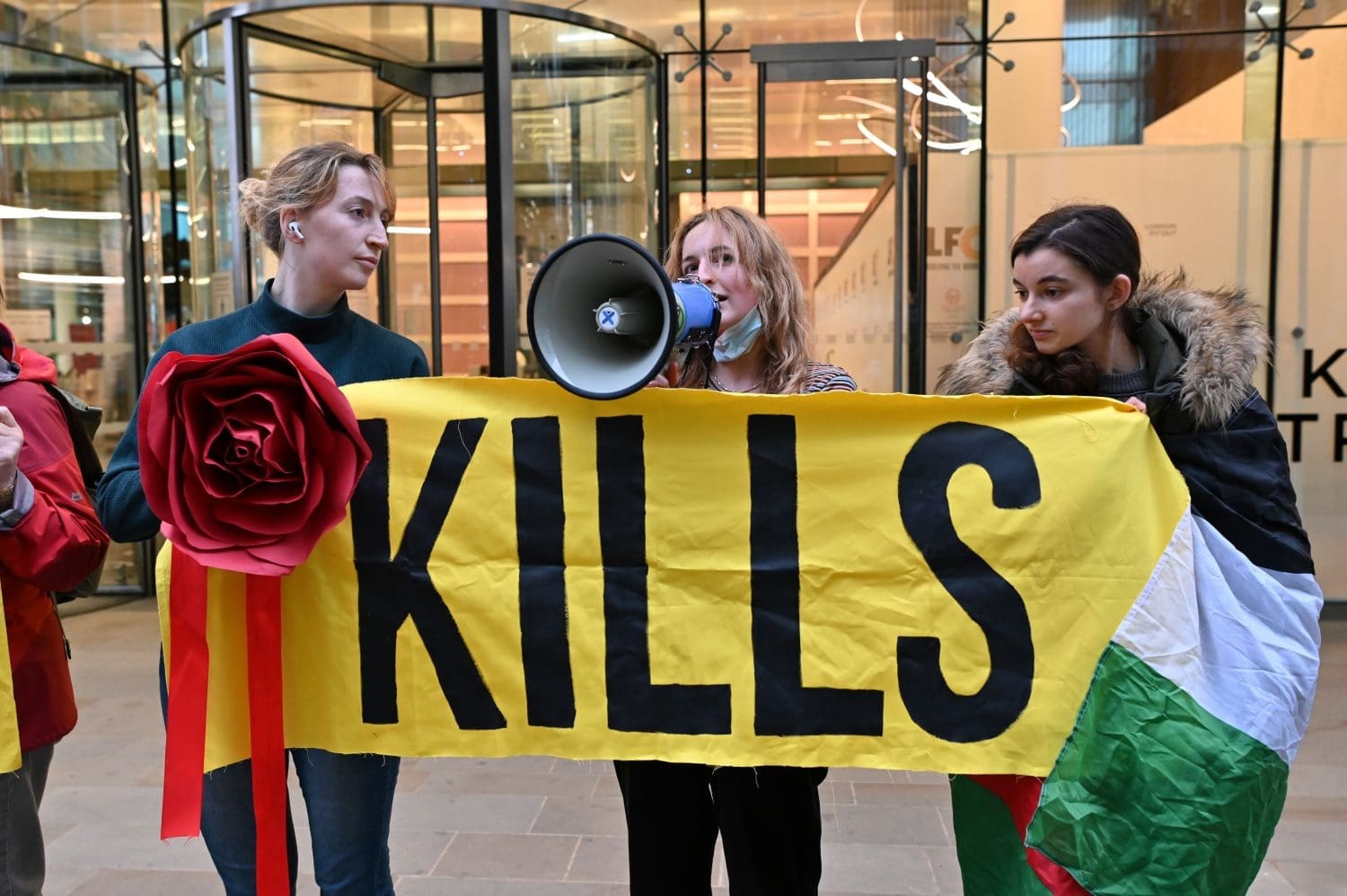 Fossil Free London activists hold one half of a banner which reads "Ithaca Kills". One protester is wrapped in the Palestinian flag. 